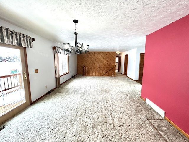 unfurnished dining area with wood walls, an inviting chandelier, a textured ceiling, and carpet flooring