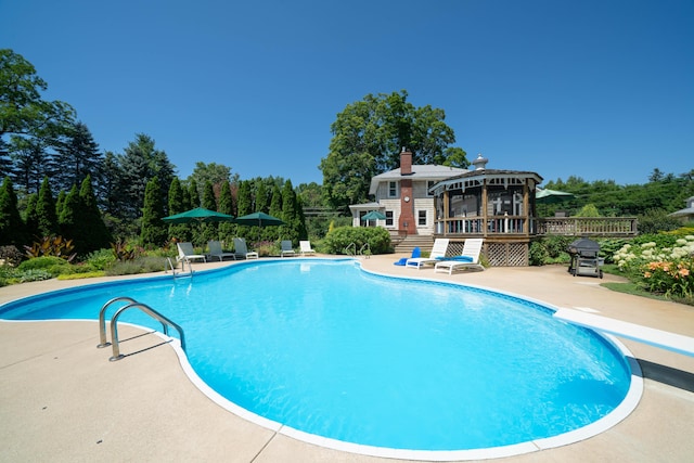 view of swimming pool featuring a diving board, a deck, and a patio