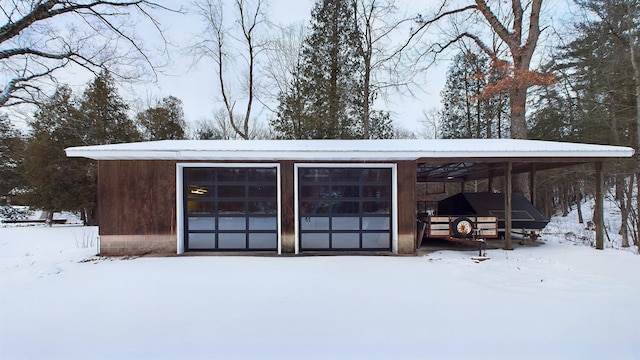 snow covered structure featuring a carport and a garage