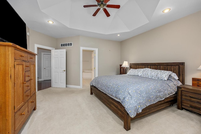 bedroom with a raised ceiling, ensuite bath, ceiling fan, and light colored carpet