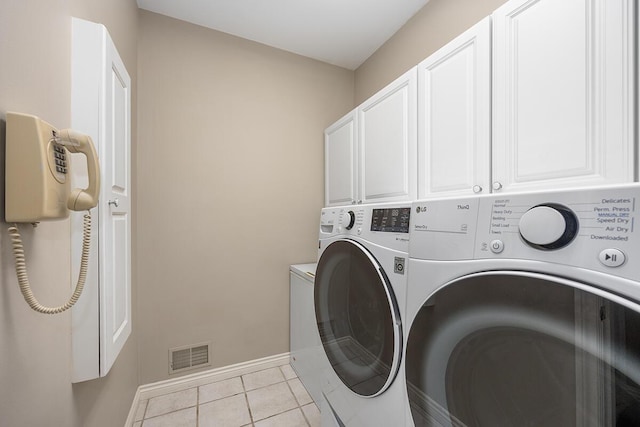 clothes washing area featuring washer and dryer, light tile patterned flooring, and cabinets