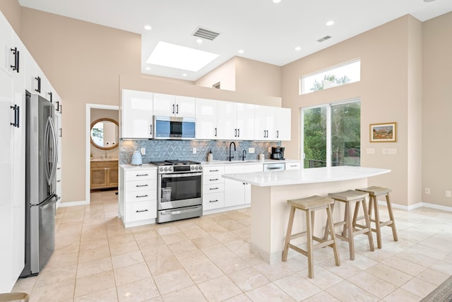 kitchen with white cabinetry, a center island, a high ceiling, decorative backsplash, and appliances with stainless steel finishes