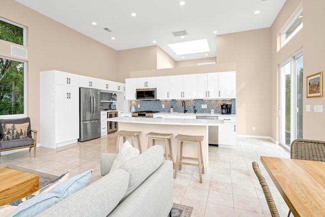 kitchen featuring a skylight, stainless steel appliances, light tile patterned floors, a high ceiling, and a kitchen island