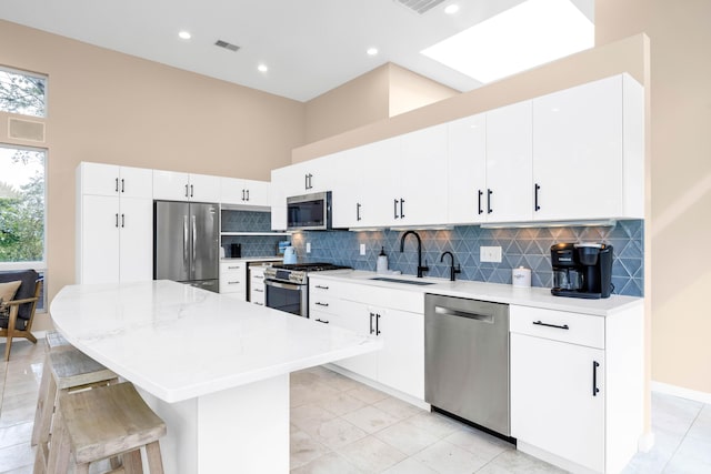 kitchen with a kitchen bar, a towering ceiling, stainless steel appliances, white cabinetry, and a kitchen island