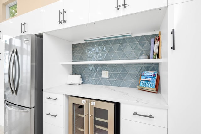 kitchen featuring tasteful backsplash, light stone counters, white cabinets, wine cooler, and stainless steel refrigerator