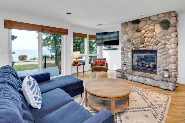 living room with hardwood / wood-style flooring, a stone fireplace, and a water view