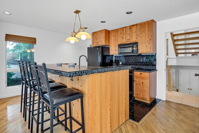 kitchen featuring hanging light fixtures, backsplash, a kitchen bar, black appliances, and hardwood / wood-style flooring