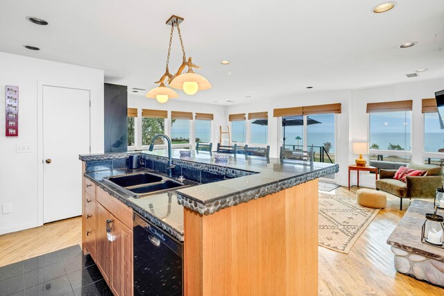 kitchen with sink, decorative light fixtures, a center island with sink, dark stone countertops, and black dishwasher