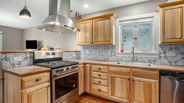 kitchen with sink, wall chimney exhaust hood, stainless steel appliances, light hardwood / wood-style floors, and decorative light fixtures