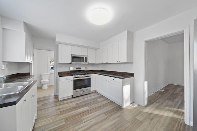 kitchen with light wood-type flooring, white cabinetry, sink, and appliances with stainless steel finishes