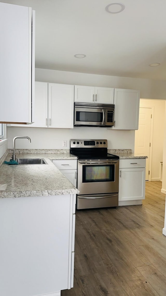 kitchen featuring hardwood / wood-style floors, stainless steel appliances, light stone counters, white cabinets, and sink