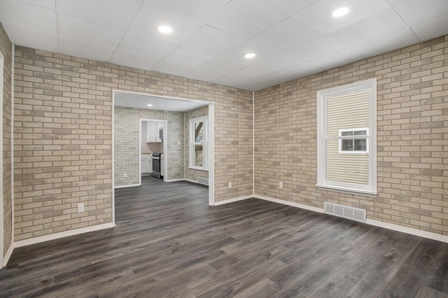 unfurnished room with a paneled ceiling, brick wall, and dark hardwood / wood-style floors