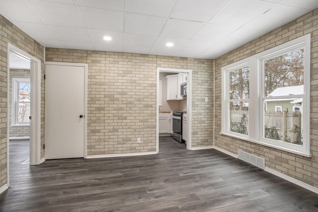 interior space with a drop ceiling, brick wall, and dark hardwood / wood-style floors