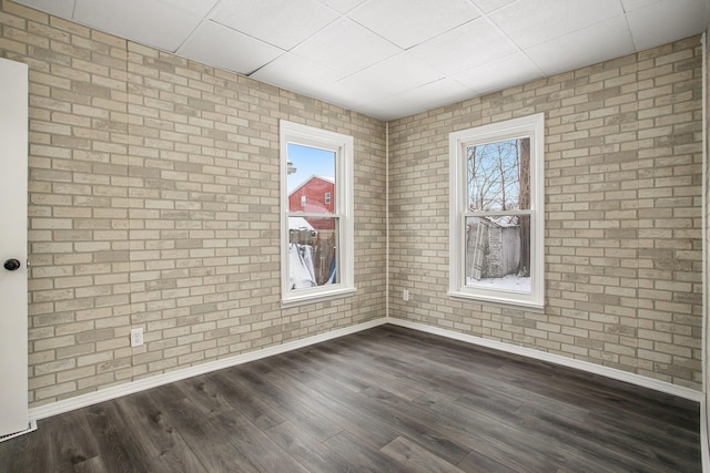 unfurnished room with dark hardwood / wood-style flooring, brick wall, and plenty of natural light