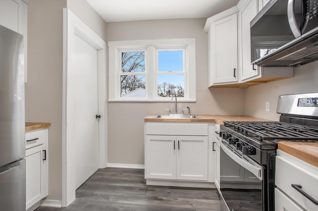 kitchen with wood counters, stainless steel appliances, sink, white cabinets, and dark hardwood / wood-style floors