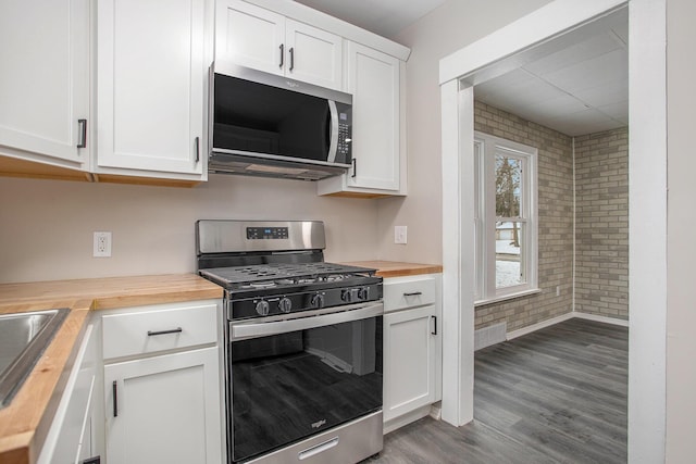 kitchen with butcher block countertops, white cabinets, stainless steel appliances, and brick wall