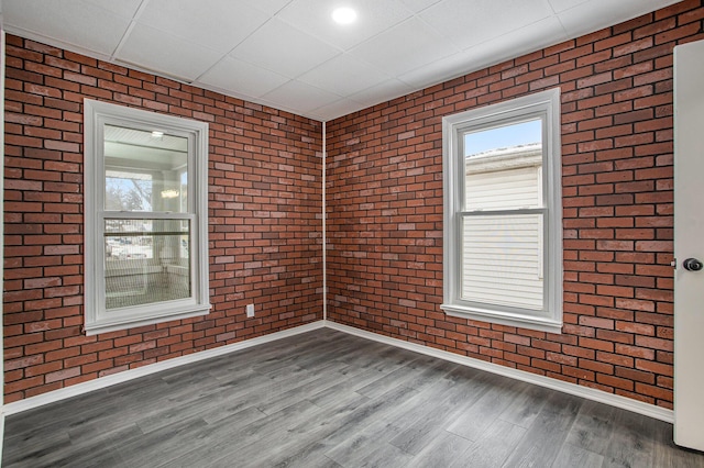 spare room featuring wood-type flooring, a paneled ceiling, and brick wall