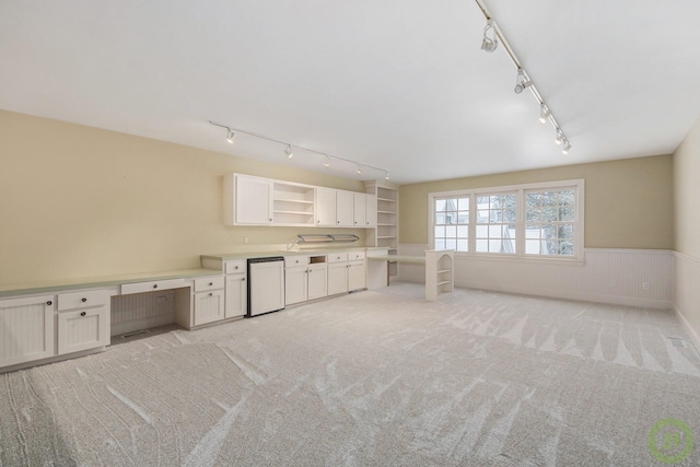 unfurnished living room with light carpet, built in desk, and rail lighting