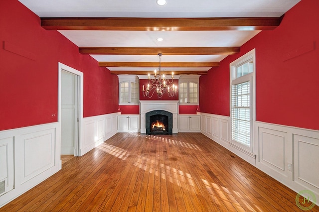 unfurnished living room featuring a notable chandelier, beamed ceiling, and light wood-type flooring