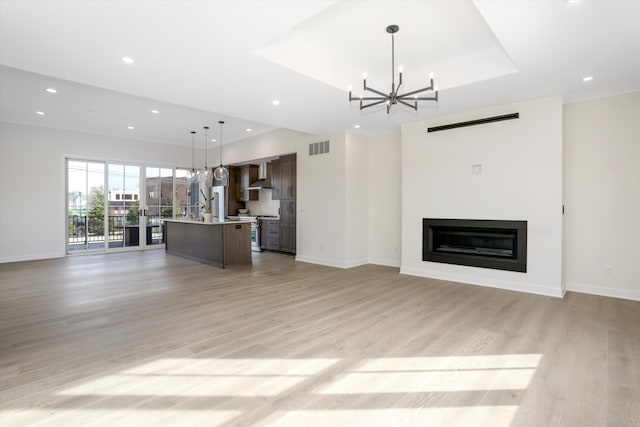 unfurnished living room featuring a raised ceiling, a chandelier, and light wood-type flooring