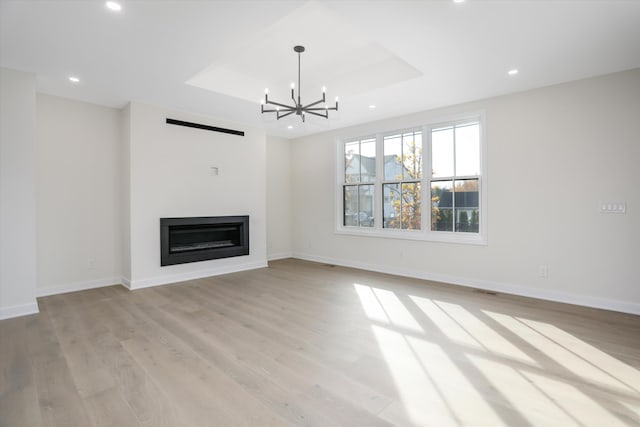 unfurnished living room featuring a chandelier, a tray ceiling, and light hardwood / wood-style flooring