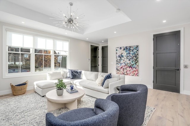 living room featuring light wood-type flooring, a tray ceiling, and an inviting chandelier