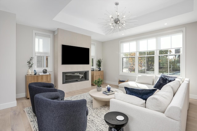 living room with a chandelier, light hardwood / wood-style flooring, and a raised ceiling