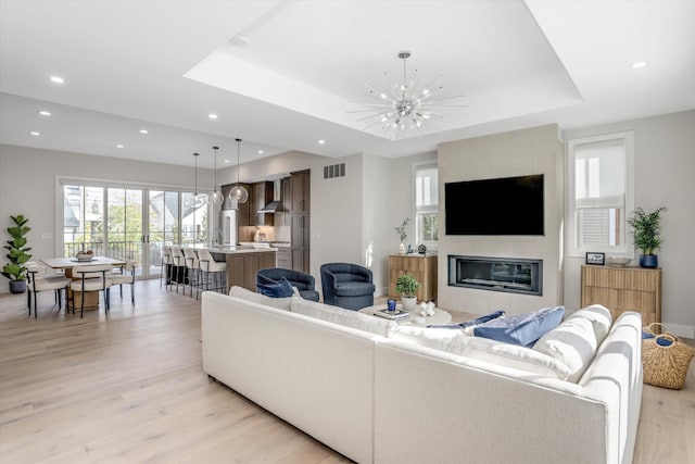 living room with a notable chandelier, light hardwood / wood-style floors, a raised ceiling, and a fireplace