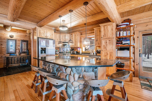 kitchen with light brown cabinets, wooden walls, hanging light fixtures, and appliances with stainless steel finishes