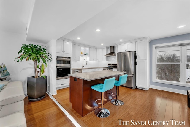 kitchen featuring white cabinets, a center island, stainless steel appliances, and wall chimney range hood