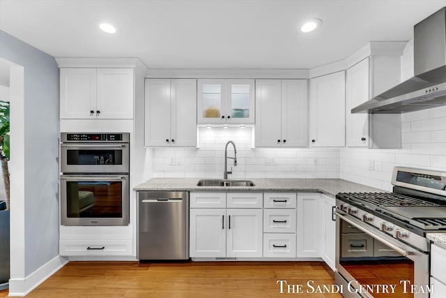 kitchen with wall chimney exhaust hood, white cabinetry, sink, and appliances with stainless steel finishes