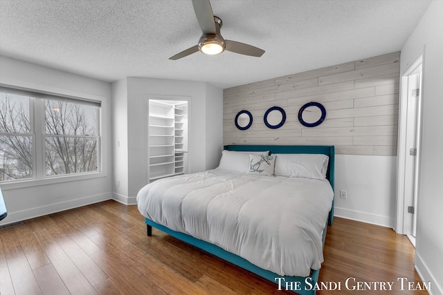 bedroom with ceiling fan, a spacious closet, hardwood / wood-style floors, a textured ceiling, and wooden walls