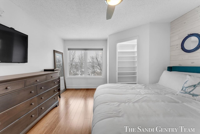 bedroom featuring a walk in closet, ceiling fan, light hardwood / wood-style flooring, and a textured ceiling