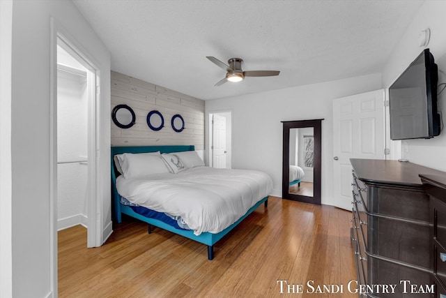 bedroom featuring wood walls, hardwood / wood-style floors, ceiling fan, and a textured ceiling