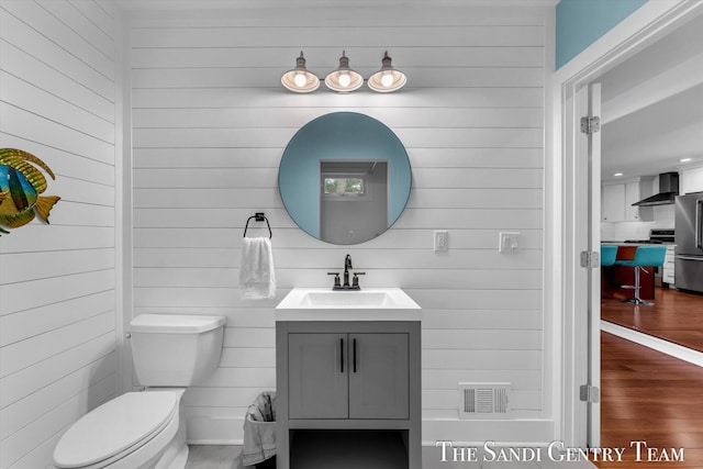 bathroom with wooden walls, vanity, and toilet