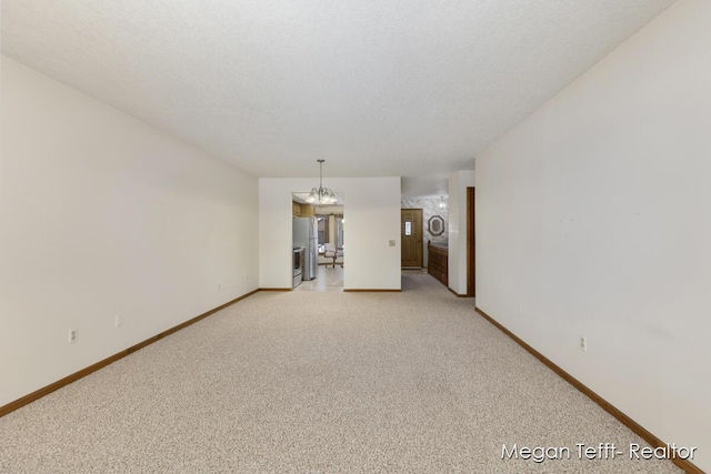 carpeted empty room with a textured ceiling and an inviting chandelier