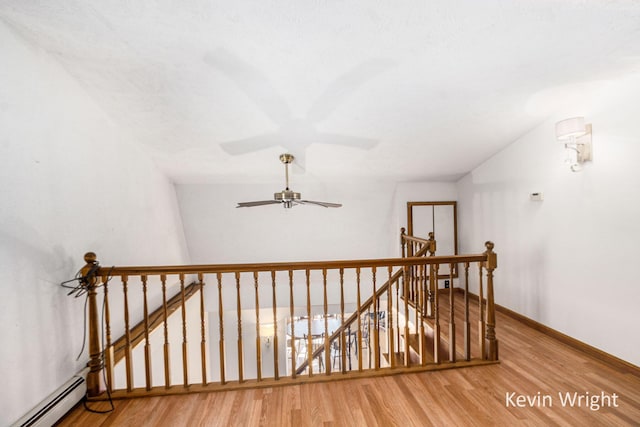 stairway with hardwood / wood-style flooring, ceiling fan, baseboard heating, and vaulted ceiling