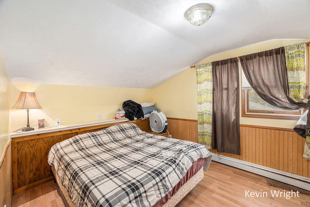 bedroom with baseboard heating, wooden walls, vaulted ceiling, and light wood-type flooring