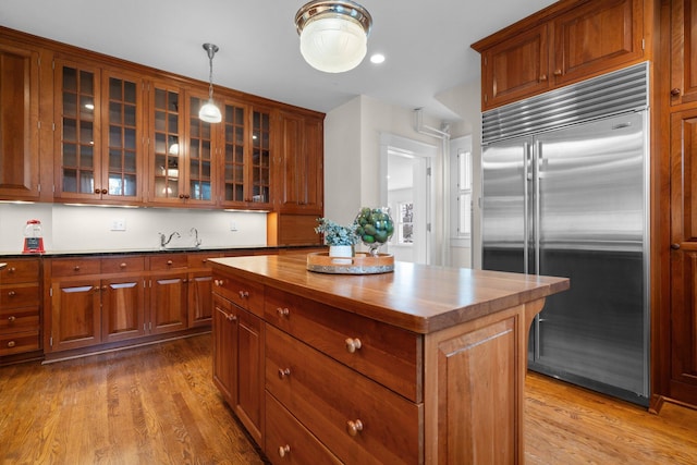 kitchen featuring pendant lighting, butcher block countertops, stainless steel built in refrigerator, a center island, and light wood-type flooring