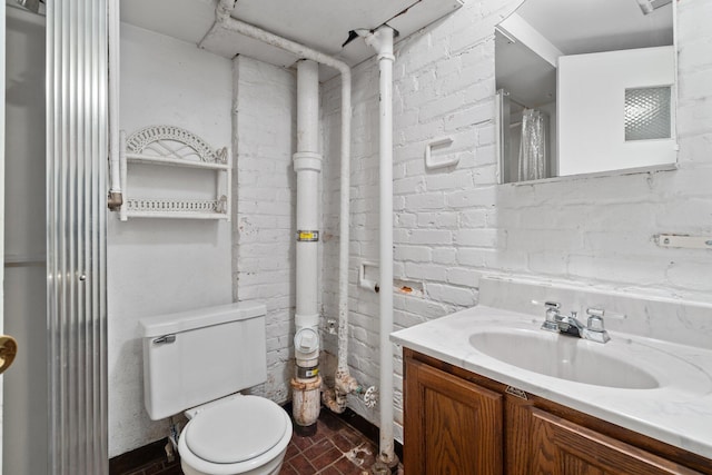 bathroom featuring vanity, brick wall, and toilet