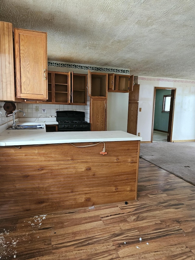 kitchen with sink, dark wood-type flooring, kitchen peninsula, black range with gas cooktop, and a textured ceiling