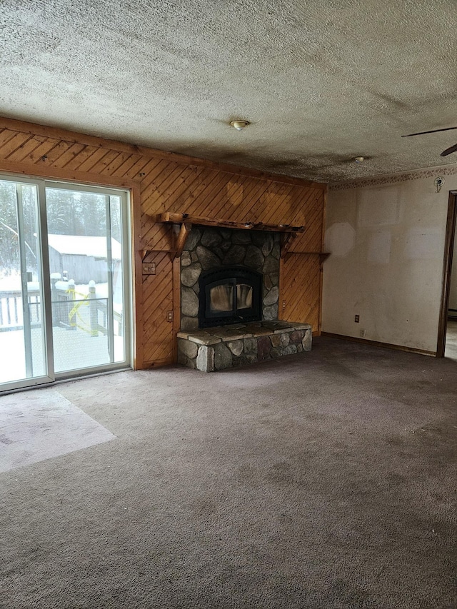 unfurnished living room featuring a textured ceiling, carpet floors, a stone fireplace, and wooden walls