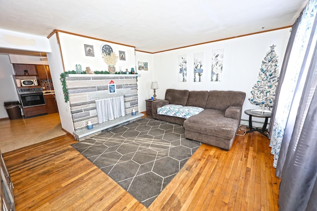 living room with wood-type flooring, ornamental molding, and a stone fireplace