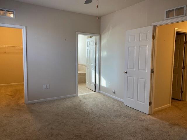 unfurnished bedroom featuring light carpet, a walk in closet, ensuite bath, ceiling fan, and a closet