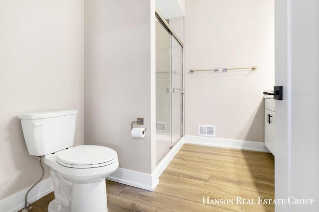 bathroom with hardwood / wood-style flooring, a shower with shower door, and toilet