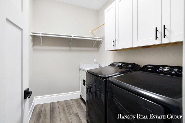 washroom featuring cabinets, sink, light hardwood / wood-style floors, and washing machine and clothes dryer