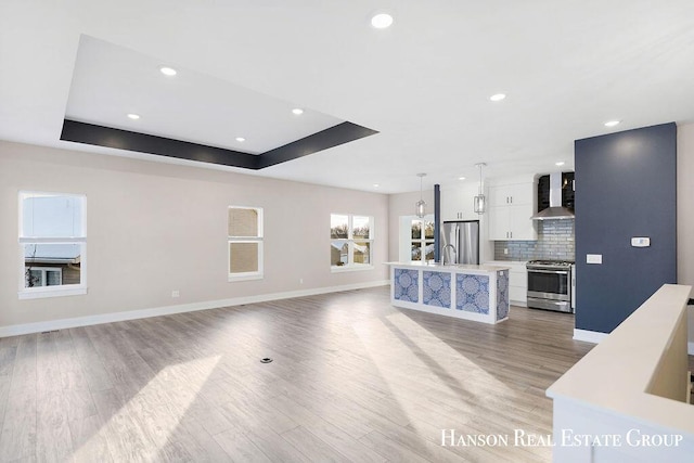 unfurnished living room featuring a raised ceiling, sink, and light hardwood / wood-style flooring