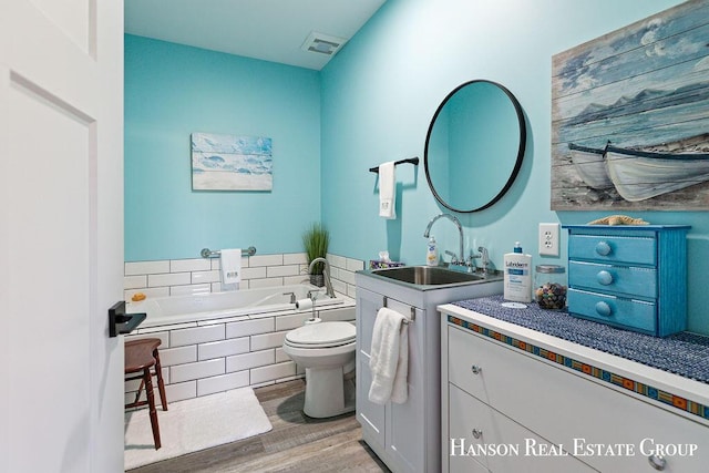 bathroom featuring vanity, toilet, wood-type flooring, and tiled bath