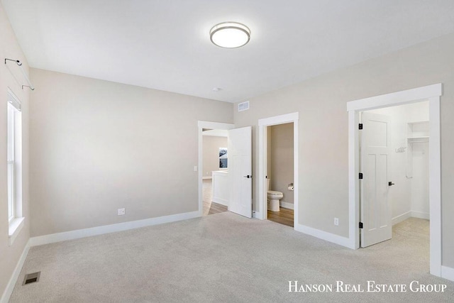 unfurnished bedroom featuring ensuite bathroom and light colored carpet