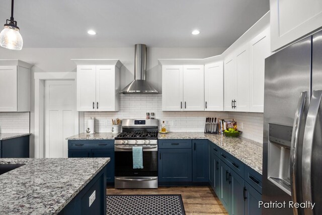 kitchen with appliances with stainless steel finishes, blue cabinetry, hanging light fixtures, wall chimney range hood, and white cabinets